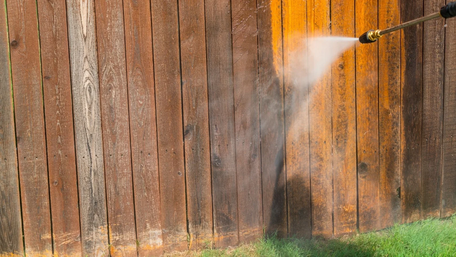 Pressure washer spraying a wood privacy fence, cleaning weathered gray boards to reveal warm natural wood tones