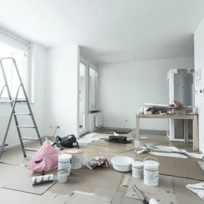Empty room with kraft paper floor protection, white paint buckets, step ladder, and painting supplies before interior painting